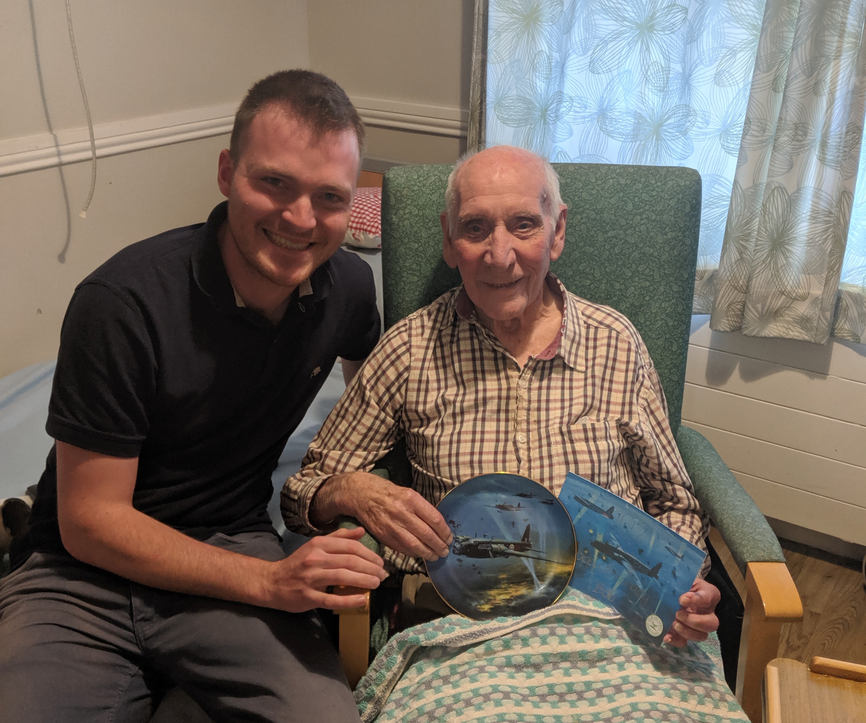 Image shows RAF veteran holding ceramic plate and picture of spitfire aircraft with civilian.